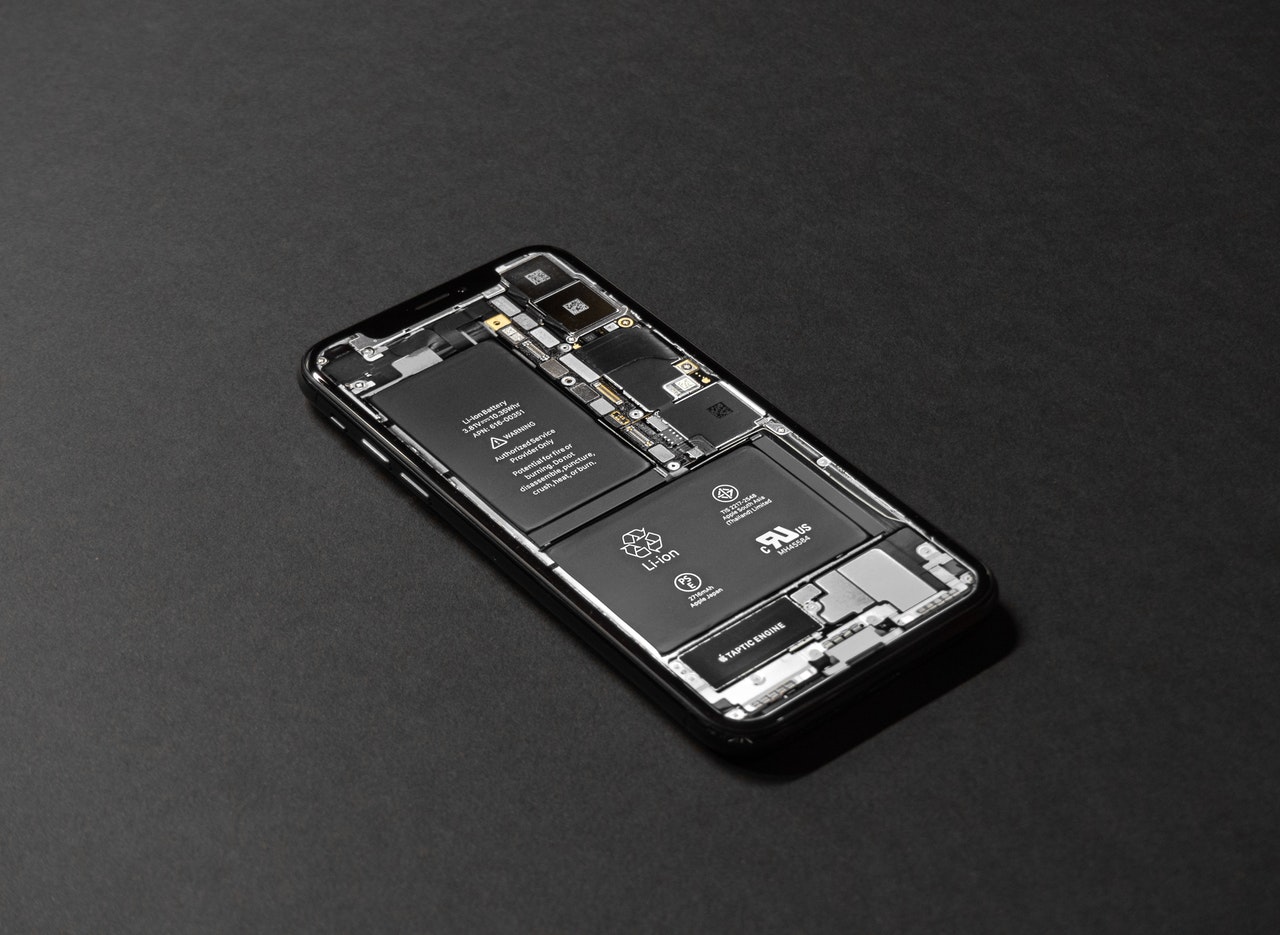A smartphone, its back cover removed, reveals internal components like the battery and circuit board on a dark surface. This intricate layout highlights the electronic parts and symbols often scrutinized in defective product injuries cases in Connecticut.