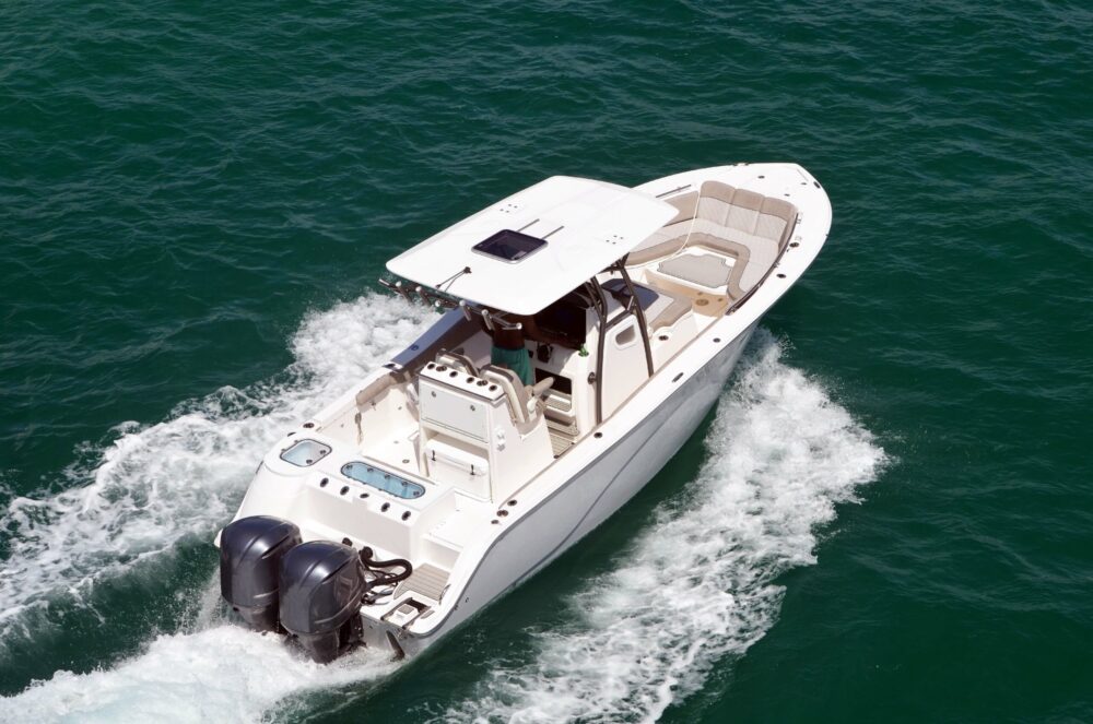 A white motorboat with dual outboard engines skillfully navigates through turquoise water, creating a wake behind it. Reminiscent of sunny days spent on the waves rather than stories of a Connecticut boating accident, it features a central console and comfortable seating area.