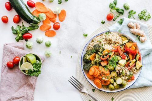 A colorful plate of quinoa with broccoli, carrots, zucchini, and red bell peppers highlights the path to recovery. Surrounding it are cherry tomatoes, carrot slices, sprouts, ginger, greens, and a small bowl with lime slices—each ingredient playing its part in restoring optimal nutrition.