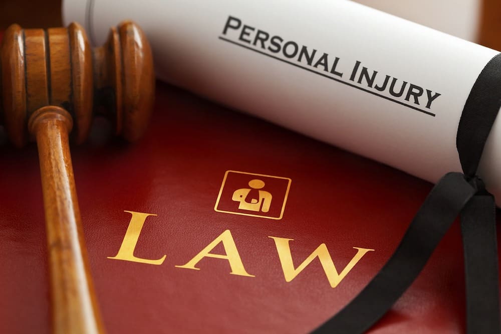 A wooden gavel rests on a red book with the word "LAW" in gold letters. Nearby, a rolled-up document labeled "Personal Injury" is tied with a black ribbon, serving as a reminder of mistakes made during car accidents.