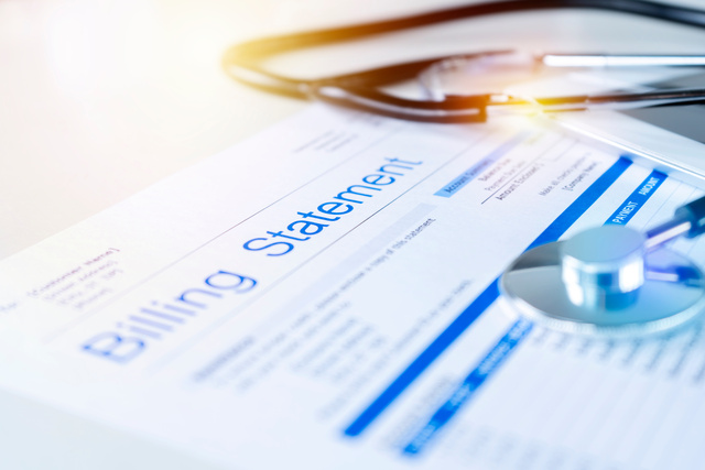 A close-up of a billing statement on a desk with a stethoscope, pen, and glasses artfully placed on top. The image conveys a healthcare financial context, highlighting medical billing, expenses, and future medical expenses in sharp focus.