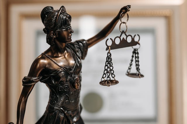 Close-up of a bronze statue of Lady Justice holding balanced scales, with a blurred certificate or legal document in the background—symbolizing fairness in Connecticut personal injury claims involving disfigurement or scarring.